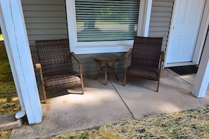 A porch with two wicker chairs and a small round table, a window with blinds, and a door. - 3 blocks to Notre Dame, EV Charger, BBQ & Fire Pit! (1707) (South Bend)