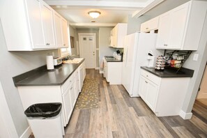 A narrow kitchen with white cabinets, a black countertop, a microwave, and a coffee maker.