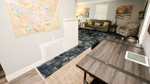 A modern living room with a large wall map, a dining area with a wooden table, and a sofa set. - 3 blocks to Notre Dame, EV Charger, BBQ & Fire Pit! (1707) (South Bend)