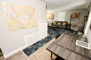 A modern living room with a large wall map, a dining area with a wooden table, and a sofa set. - 3 blocks to Notre Dame, EV Charger, BBQ & Fire Pit! (1707) (South Bend)