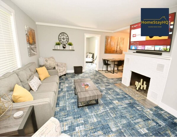 A living room with a sofa, coffee table, fireplace, and a television displaying a website. - 3 blocks to ND, EV charger, bbq & fire pit! (1707) (South Bend)