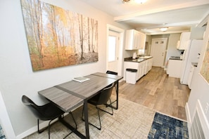 A modern kitchen with white cabinets, a dining area with a table and chairs, and a large painting on the wall. - 3 blocks to Notre Dame, EV Charger, BBQ & Fire Pit! (1707) (South Bend)