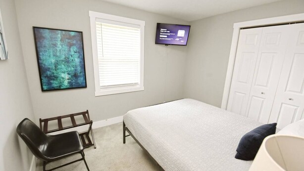 A bedroom with a bed, a desk, a chair, a TV, and a door. - 3 blocks to Notre Dame, EV Charger, BBQ & Fire Pit! (1707) (South Bend)