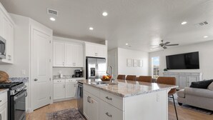 A modern kitchen with white cabinets, a central island, and a dining area with a gray sofa. - The One by the Pool: Waterslide, Lazy River, Pickleball, Shuffleboard! (Washington)