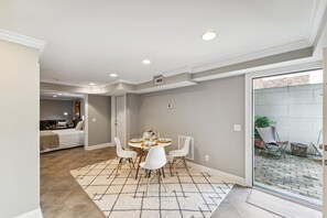 A dining area with a round table and white chairs, a kitchen in the background, and a view of the outside through a glass door. - West Taylor Garden Retreat (Savannah)
