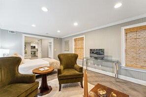 A modern hotel room with a bed, a green armchair, a small round table, a TV on a glass stand, and a window with blinds. - West Taylor Garden Retreat (Savannah)