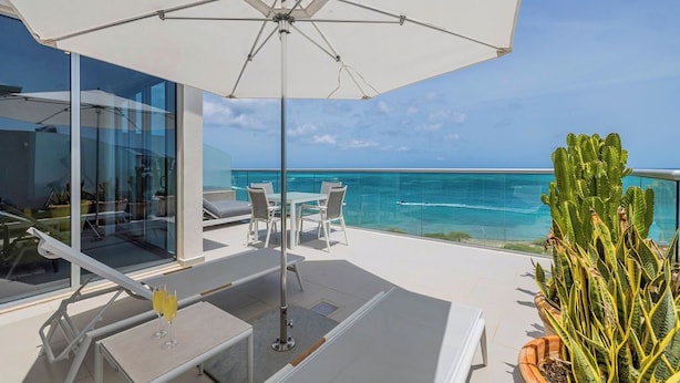 Un balcon avec une balustrade en verre, une table avec deux verres, un parasol blanc et une plante en pot.