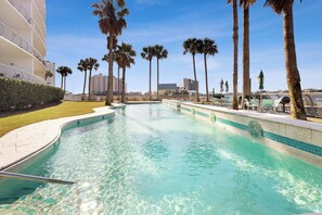 A clear swimming pool surrounded by palm trees and a building with balconies.