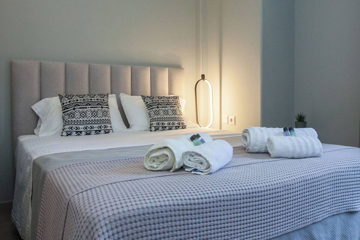 A neatly made bed with patterned pillows, a folded towel, and a bedside lamp.