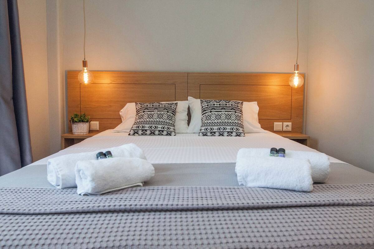A neatly made bed with patterned pillows, a bedside plant, and two towels.