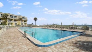 A swimming pool with a tiled edge, surrounded by lounge chairs and a brick patio.