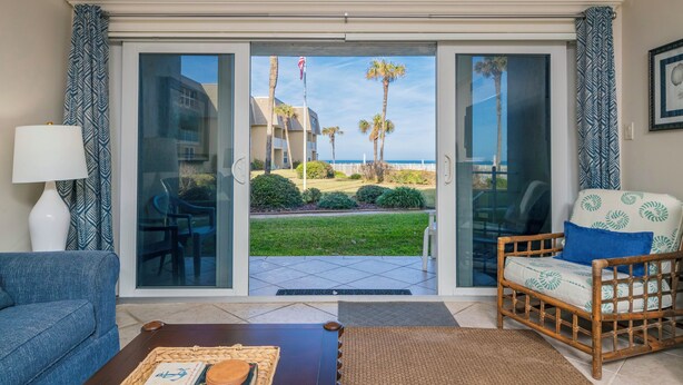 A hotel room with a view of the beach, a sofa, a chair, and a coffee table.