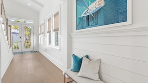 A hallway with a bench, a door with glass panels, and a painting of a boat on water. - Spacious New Home in Blue Mountain Beach (Santa Rosa Beach)