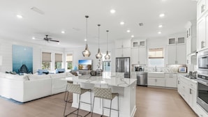 A modern kitchen with white cabinetry, a central island with bar stools, stainless steel appliances, and pendant lighting. - Spacious New Home in Blue Mountain Beach (Santa Rosa Beach)