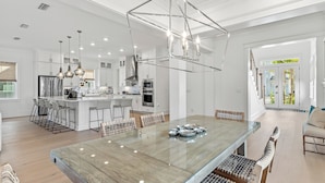 A modern kitchen with a central island, stainless steel appliances, and a glass-top dining table. - Spacious New Home in Blue Mountain Beach (Santa Rosa Beach)