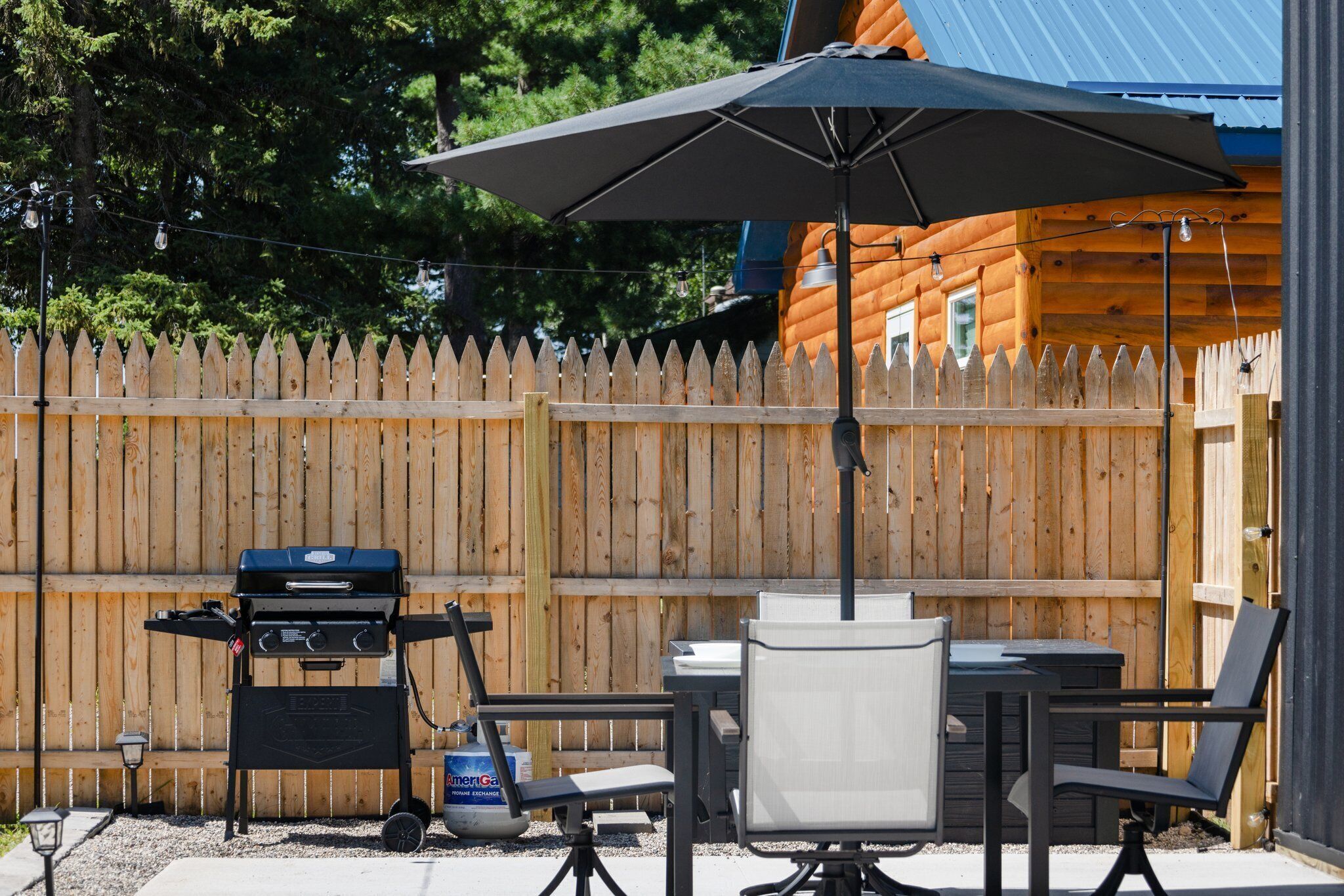 Una veranda con barbecue, tavolo e sedie da esterno e un ombrellone.