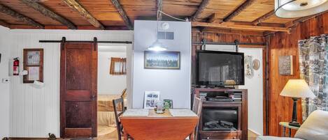 Een gezellige woonkamer met een houten plafond, een eettafel met stoelen, een televisie en een open haard.
