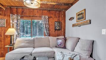 A cozy cabin interior with a sectional sofa, a lamp, a framed picture, and a window with curtains.