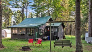 A rustic cabin with a green roof, a porch with red chairs, and a swing. - Rustic Willow Retreat - Outdoor Adventures 2 Bedroom Cabin by RedAwning (Hazelhurst)