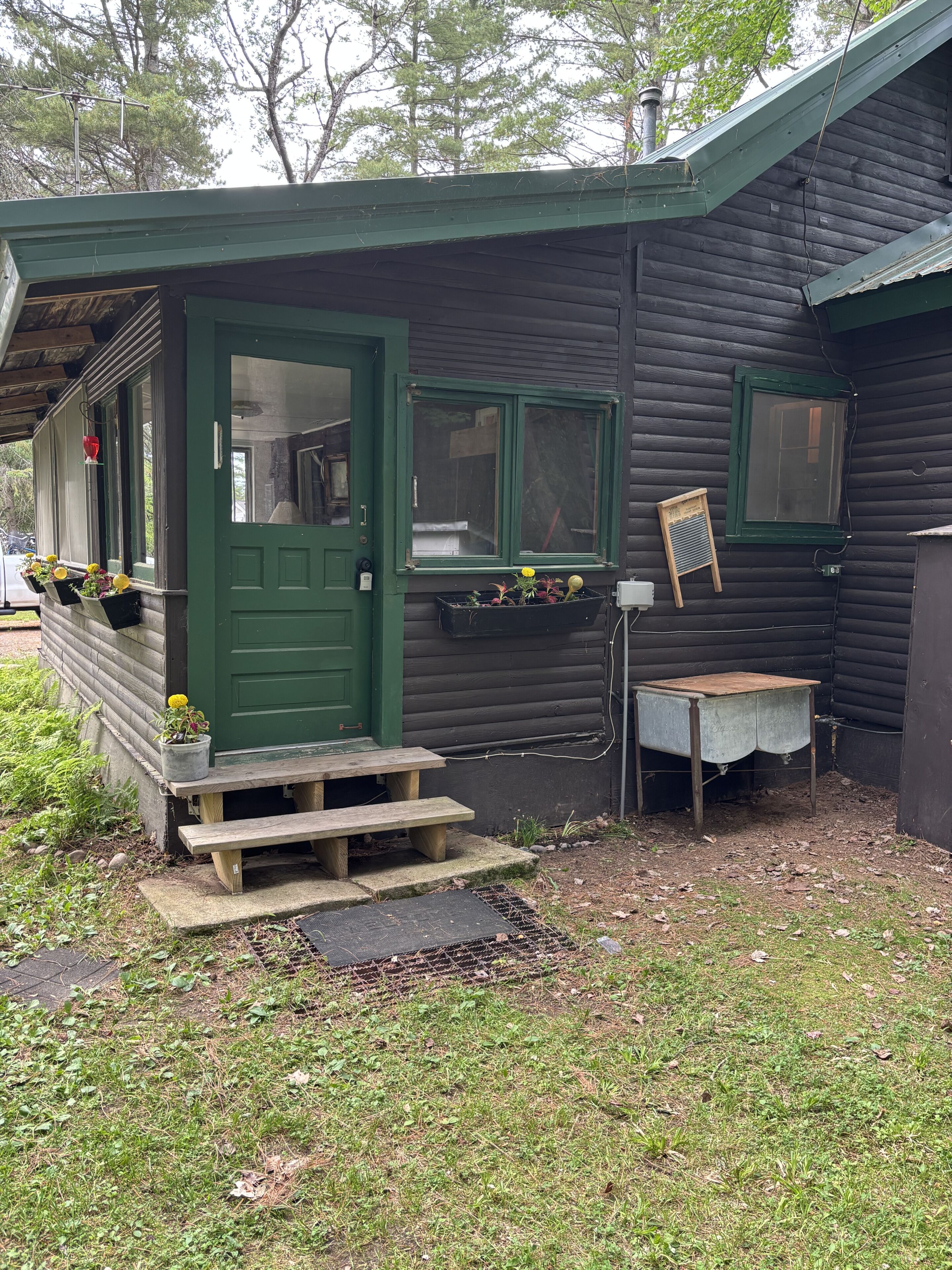 A small wooden cabin with a green door, a window with a green frame, and a wooden bench outside.