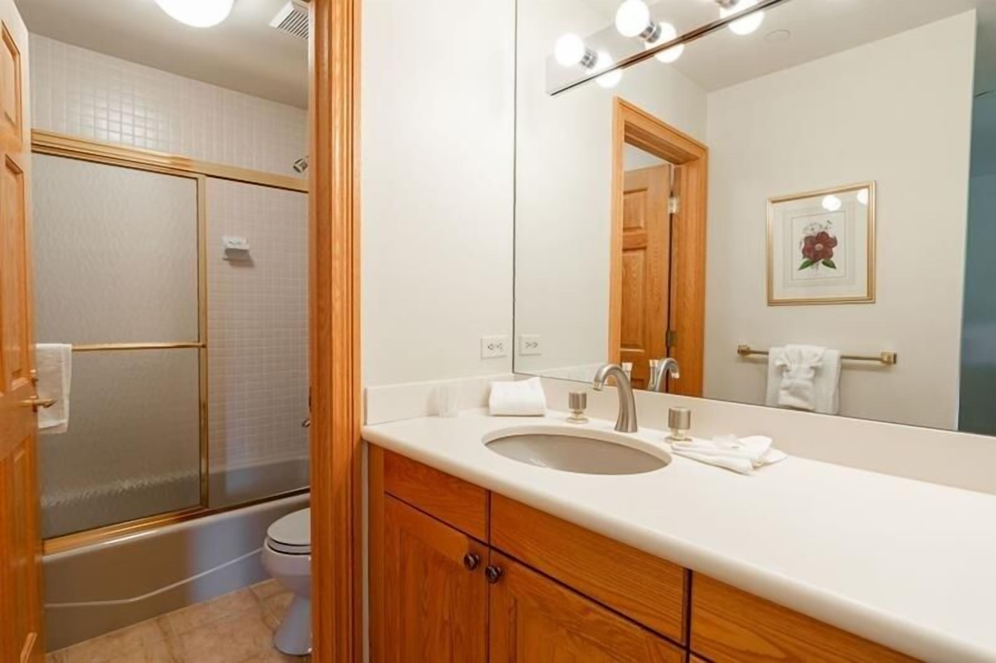 Une salle de bain moderne avec une douche à parois de verre, un lavabo blanc avec un miroir et des meubles en bois.