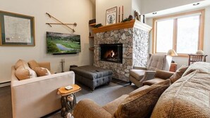A cozy living room with a stone fireplace, a large flat-screen TV, and comfortable seating. - Strawberry Park #603 4 Bedroom Condo by RedAwning (Avon)