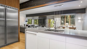 A modern kitchen with a stainless steel refrigerator, white cabinetry, and a large island with a sink.