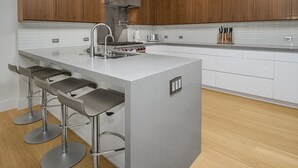 A modern kitchen with wooden cabinets, a central island with bar stools, stainless steel appliances, and a white countertop.