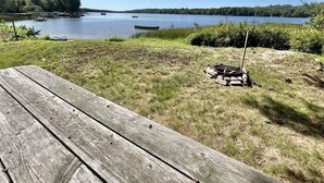 A wooden deck overlooking a lake with boats, surrounded by trees and a grassy area. - Boomfish Limit 5 2 Bedroom Cottage by RedAwning (Windham)