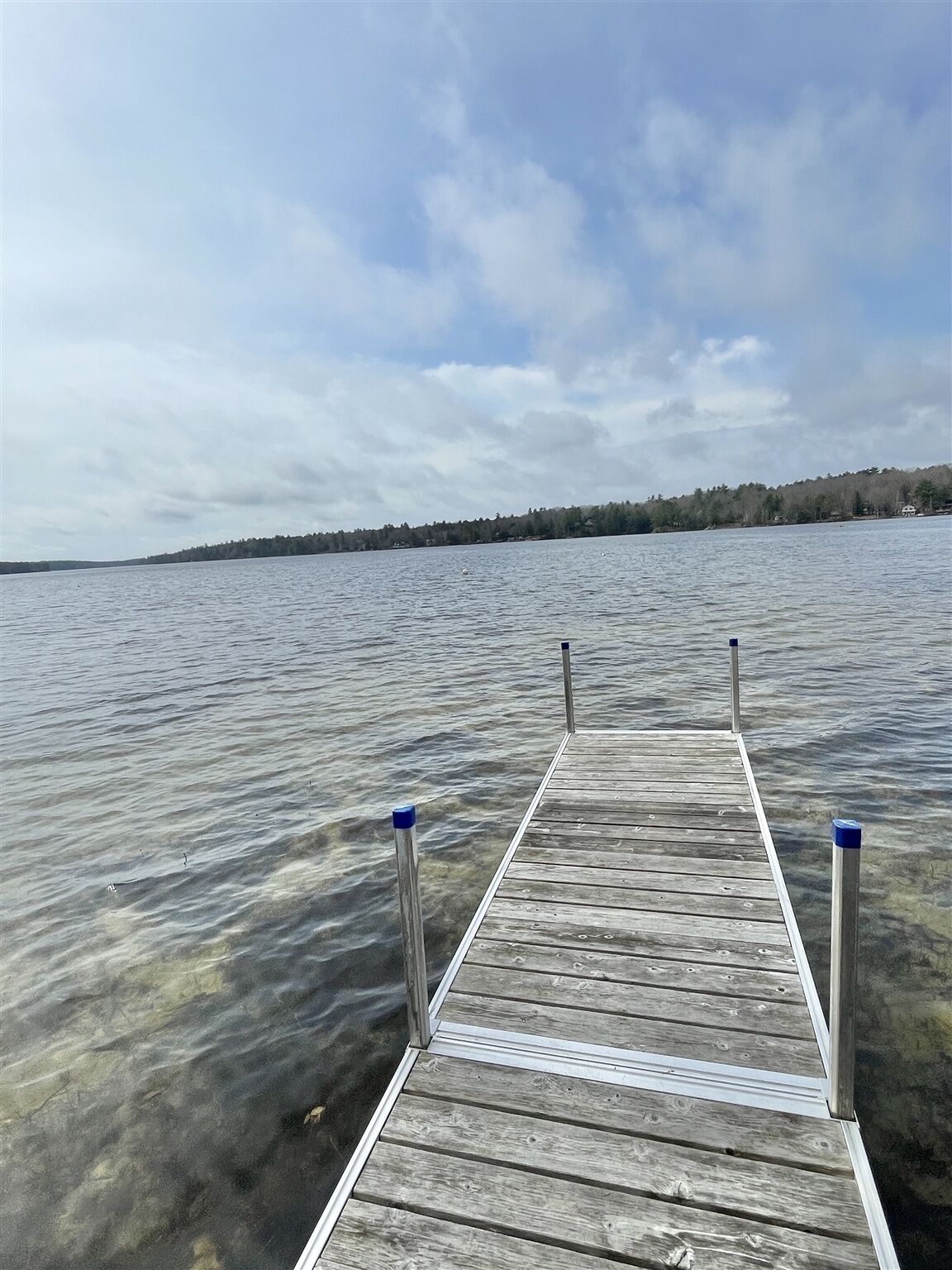 Une jetée en bois s’étendant sur une étendue d’eau calme, avec une rive visible au loin.