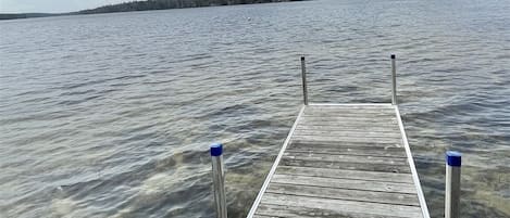 Une jetée en bois s’étendant sur une étendue d’eau calme, avec une rive visible au loin.