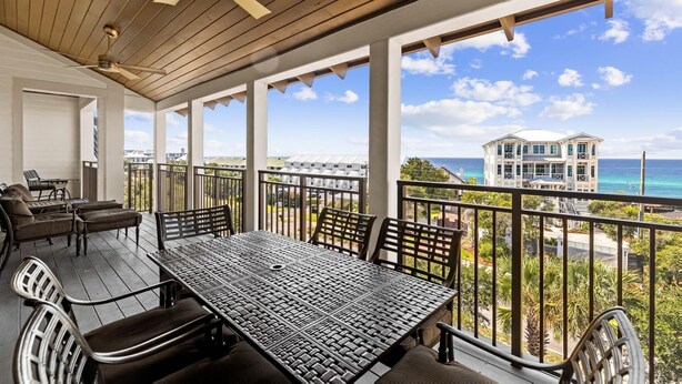 Ein überdachter Außenbereich mit Tisch und Stühlen, einem Deckenventilator und Blick auf Strand und Meer.