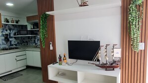 Un salon moderne avec un téléviseur à écran plat, des murs recouverts de panneaux en bois et une cuisine en arrière-plan.