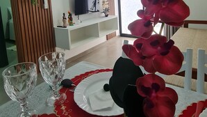 Un coin repas avec une table dressée pour deux personnes, un téléviseur et une plante décorative.