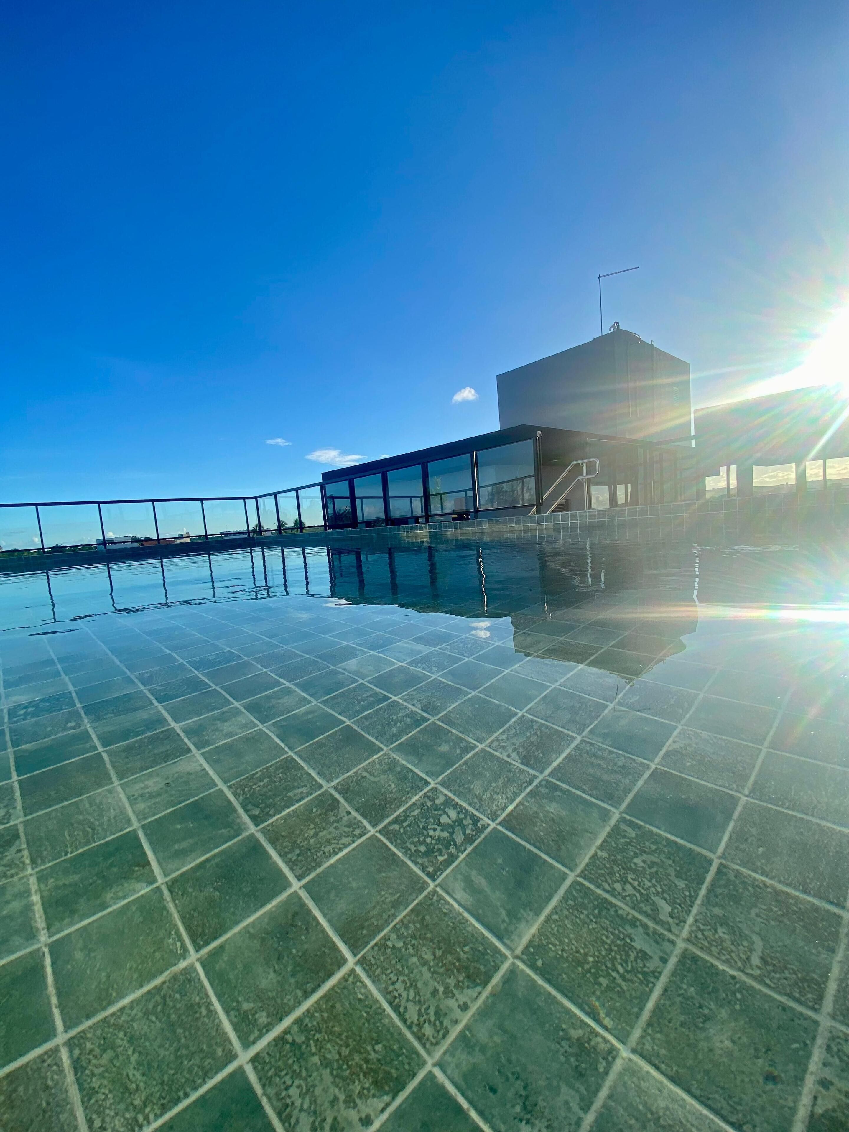 A swimming pool with clear water reflecting the sky and a modern building with large windows in the background.