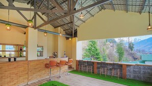 A modern bar area with wooden counters and bar stools, a stone wall, and a view of mountains. - Aatmayog Luxury Manor Manali by Blueko Hotels (Manali)