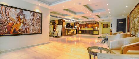 A spacious lobby with a reception desk, seating area, and a large Buddha painting on the wall.