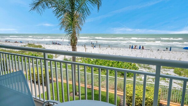 Un balcon avec vue sur la plage, les palmiers et un ciel dégagé.