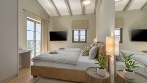 A bedroom with a large bed, two bedside tables with lamps, a TV mounted on the wall, and a window with curtains.