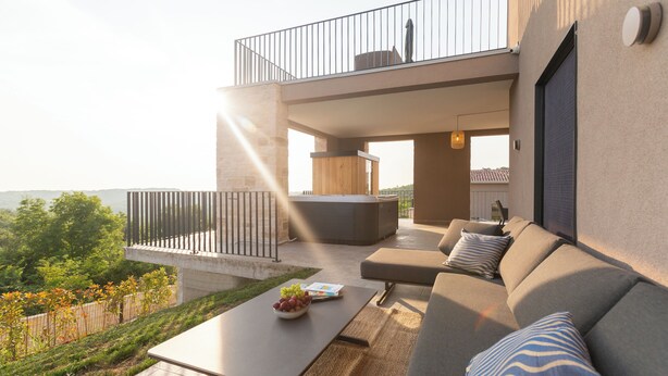 A modern outdoor living area with a sofa, a table with a bowl of fruit, and a hot tub.
