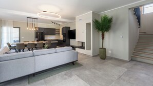 A modern living room with a grey sofa, dining area, kitchen, and a staircase.