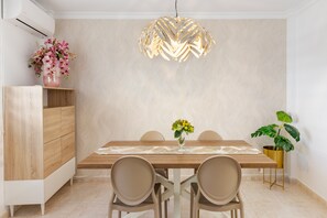 Ein Essbereich mit einem Holztisch, beigen Stühlen, einer dekorativen Hängelampe, einer Blumenvase und einer Pflanze im goldfarbenen Topf.