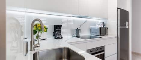 A modern kitchen with a stainless steel sink, a coffee maker, a microwave, and a refrigerator.