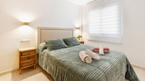 A bedroom with a bed, bedside tables, a nightstand, a window with blinds, and a wall-mounted light fixture. - Apartment 'El Corazon De Aguilas' with Wi-Fi and Air Conditioning (Águilas)