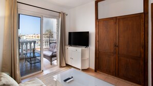 Una habitación con balcón, televisión sobre un mueble, sofá y puerta corredera.
