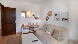 Un salón con puerta de madera, sofá blanco, mesa de centro, lámpara, espejo y sombreros colgados en la pared.