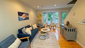 A modern living room with a blue sofa, a dining table with chairs, and a kitchen area with a gray cabinet.