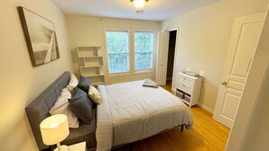 A bedroom with a bed, bedside table, lamp, and a window with blinds.