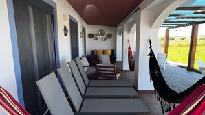 Un espacio al aire libre con techo, que incluye una hamaca, sillas acolchadas y vistas al exterior.