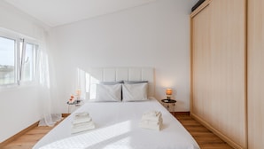 Habitación de hotel con una cama grande, una mesita de noche con lámpara, un armario y una ventana con cortinas translúcidas.